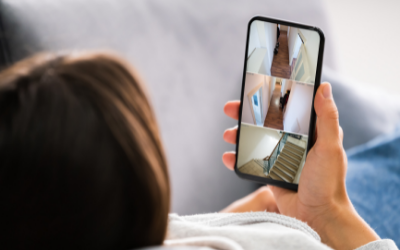 A person relaxing on a couch checks home security camera feeds on their smartphone.