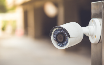 A white security camera mounted on a metal pole, viewed at an angle with a blurred background.