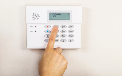 A finger presses a button on a white wall-mounted home security alarm keypad.