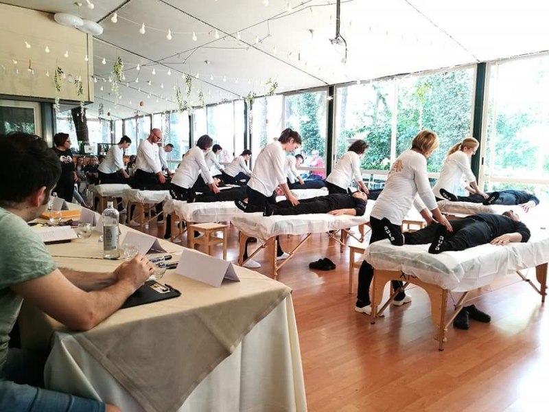 Un gruppo di persone è seduto ai tavoli in una stanza e riceve dei massaggi.