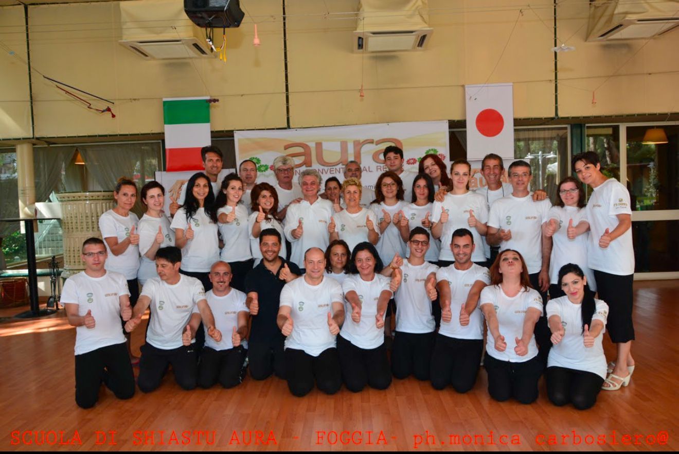 Un folto gruppo di persone in posa per una foto davanti a un cartello che dice aura