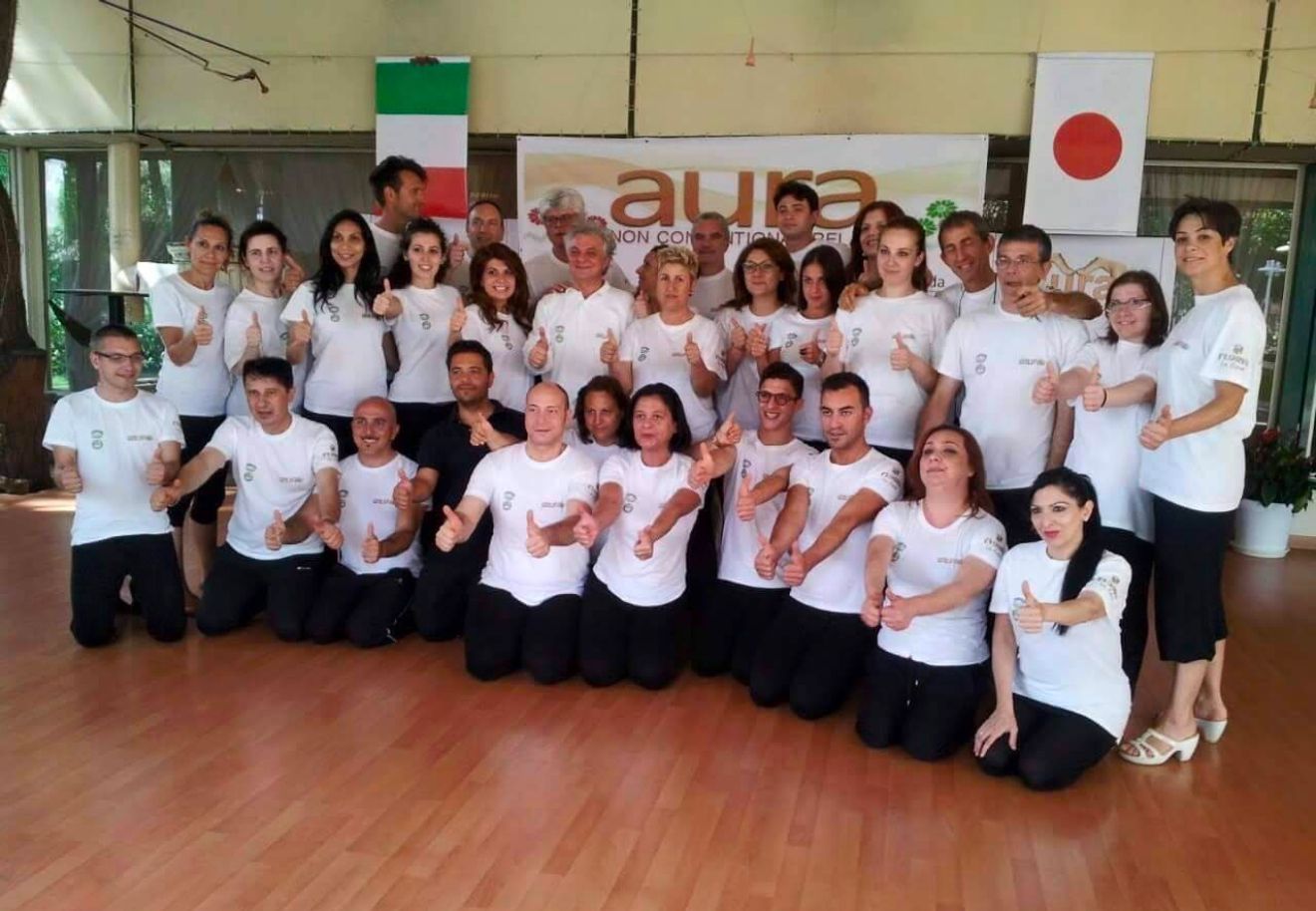 Un folto gruppo di persone in posa per una foto davanti a un cartello che dice aura