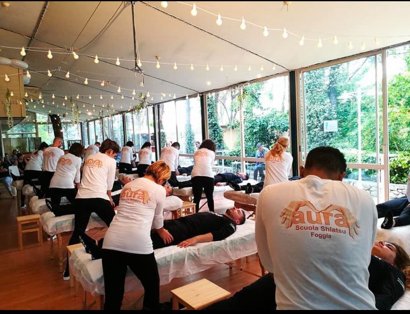 Un gruppo di persone sta ricevendo massaggi in una stanza con molte finestre.