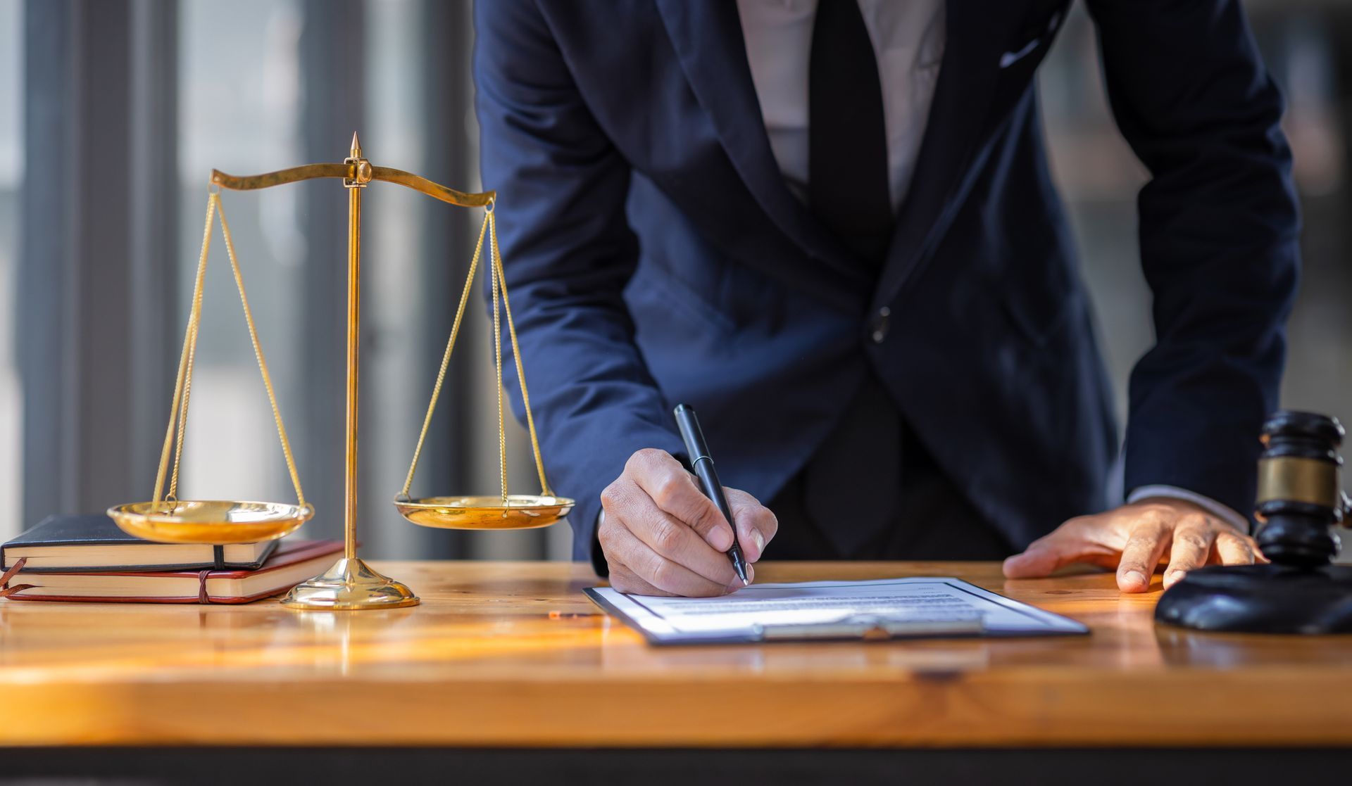 A lawyer is signing a document at a desk with scales of justice and a judge 's gavel.