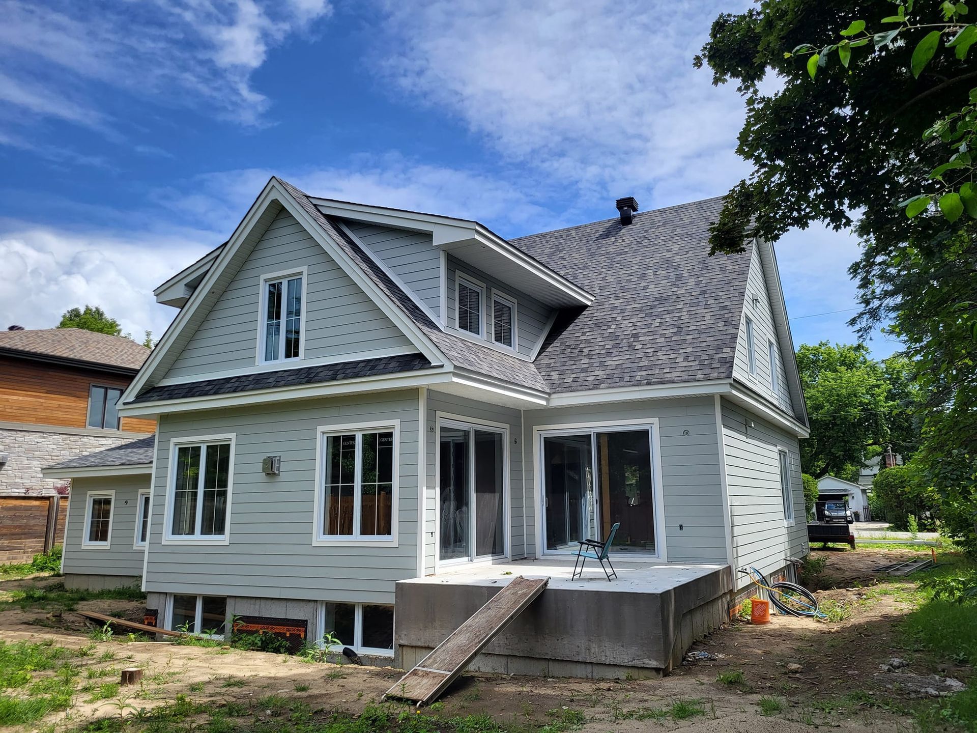 Une grande maison blanche avec un toit gris est assise au sommet d'un champ de terre.