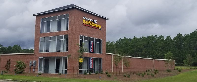 A three-story brick building with large windows and a sign, surrounded by a brick wall and trees.