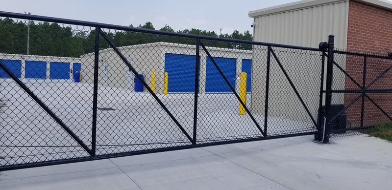 Chain link fence gate in front of a storage facility with blue doors.
