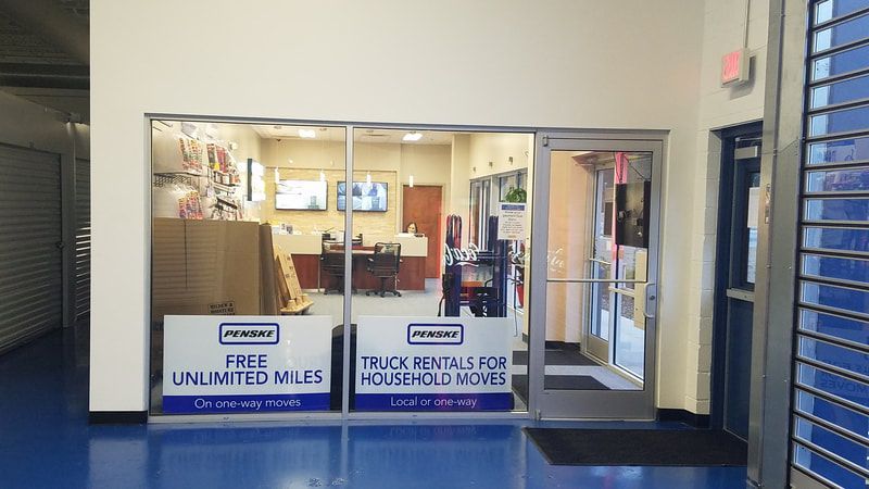 A rental office with glass windows, offering free unlimited miles and truck rentals. Blue floor and white walls.