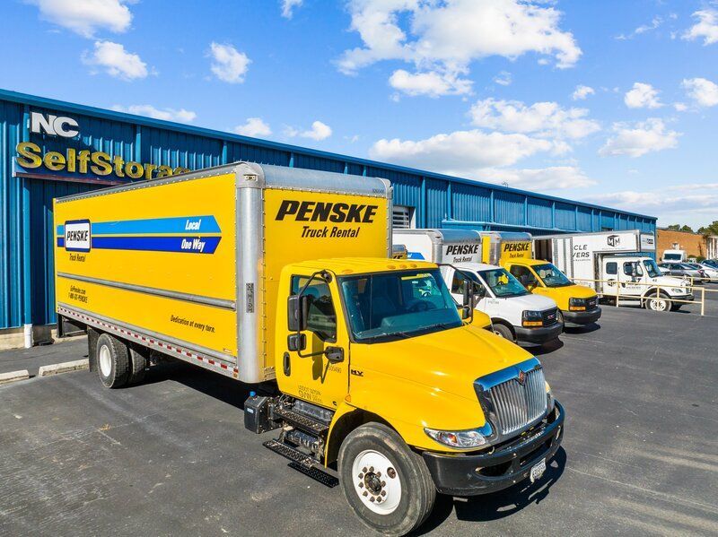 Yellow Penske truck parked in front of a NC Self Storage building with other trucks.