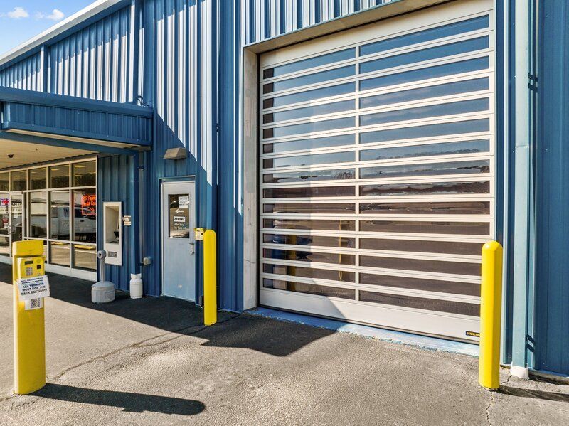 Blue industrial building with a large transparent door and yellow safety bollards.