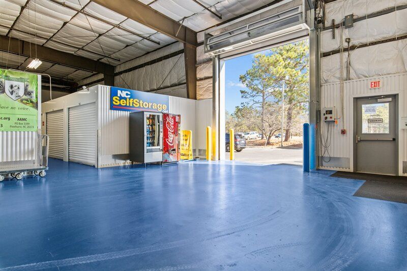 Interior of a storage facility with blue floors, storage units, vending machine, and open bay door.