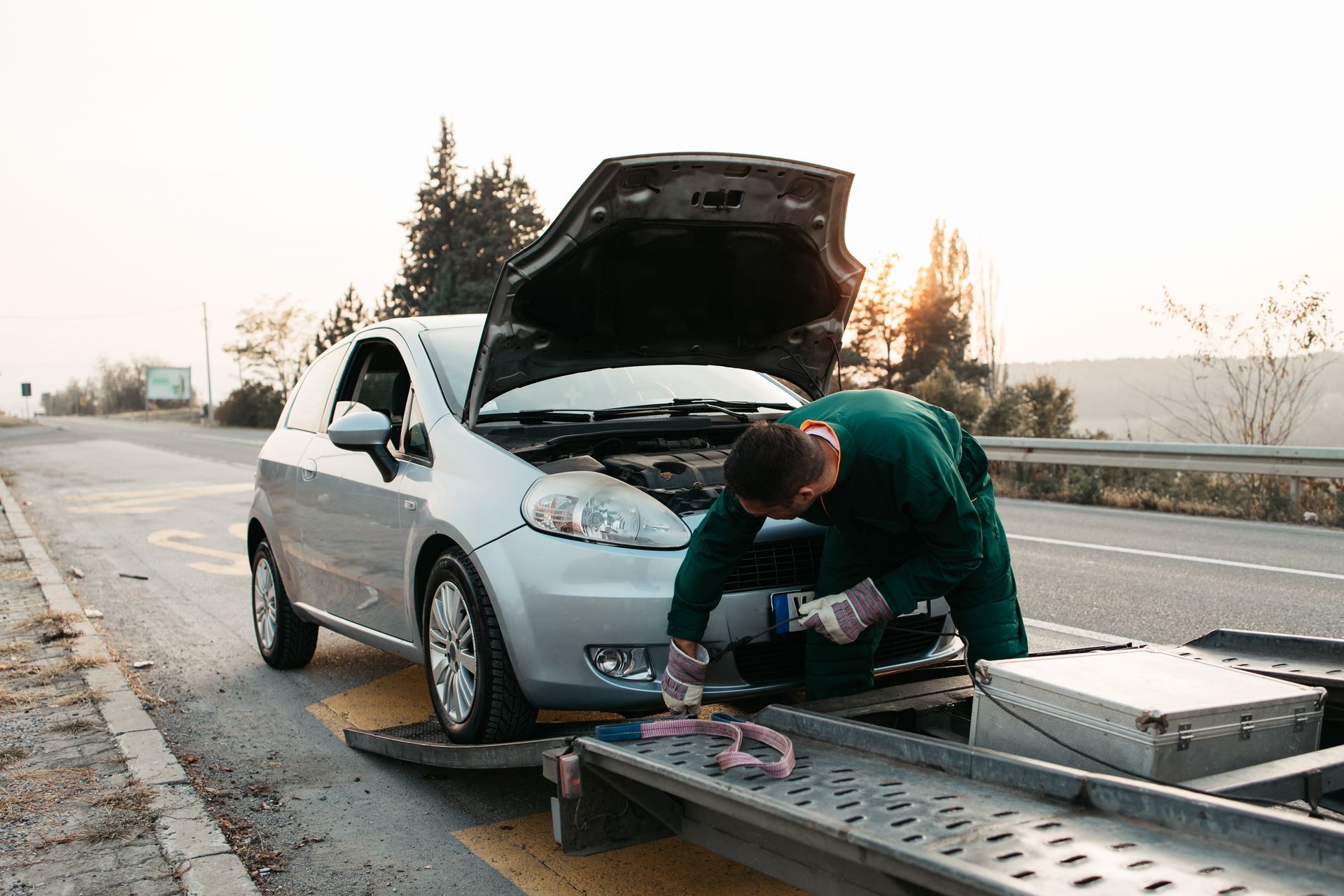 A towing worker securing a broken down car onto a roadside tow truck. A towing worker securing a broken down car onto a roadside tow truck.