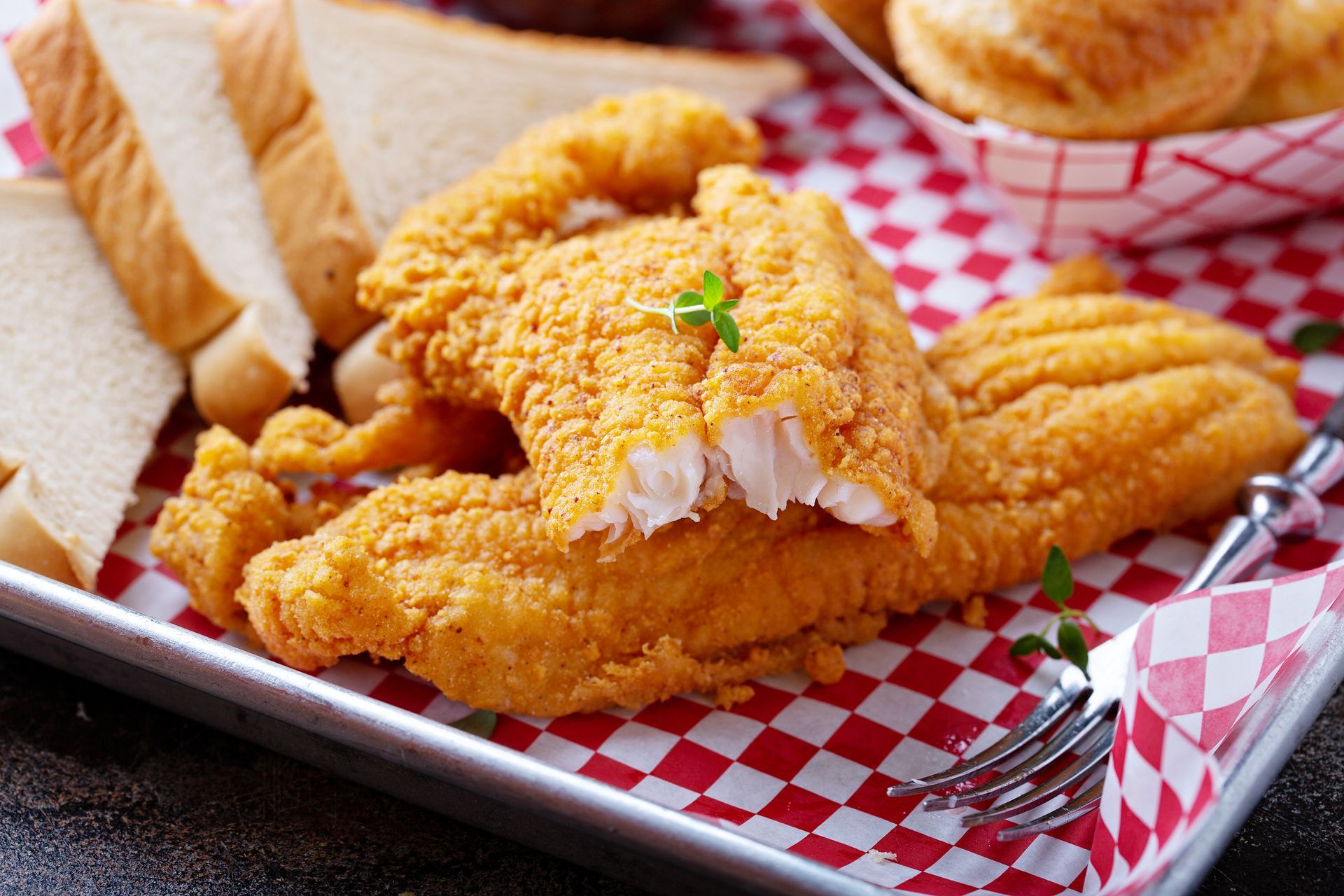 Fried fish fillets on a red checkered tray with bread and rolls.