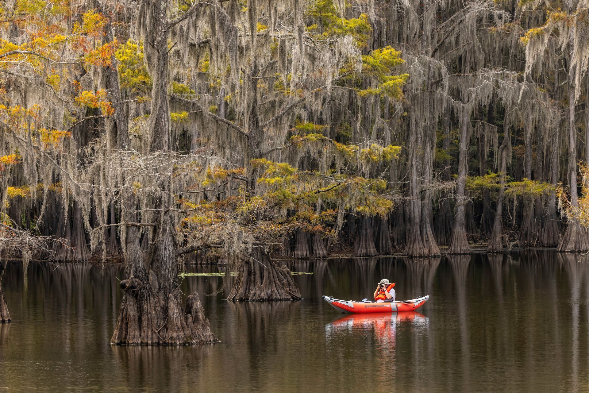 A person is paddling a red kayak on a lake surrounded by trees.