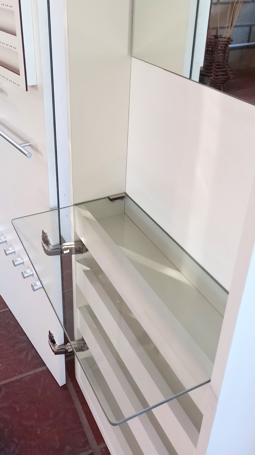 Estantería de cristal con fondo blanco y soportes metálicos junto a una puerta.