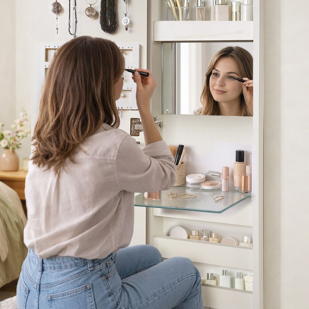 Mujer aplicándose maquillaje frente a un espejo de tocador en un dormitorio luminoso.