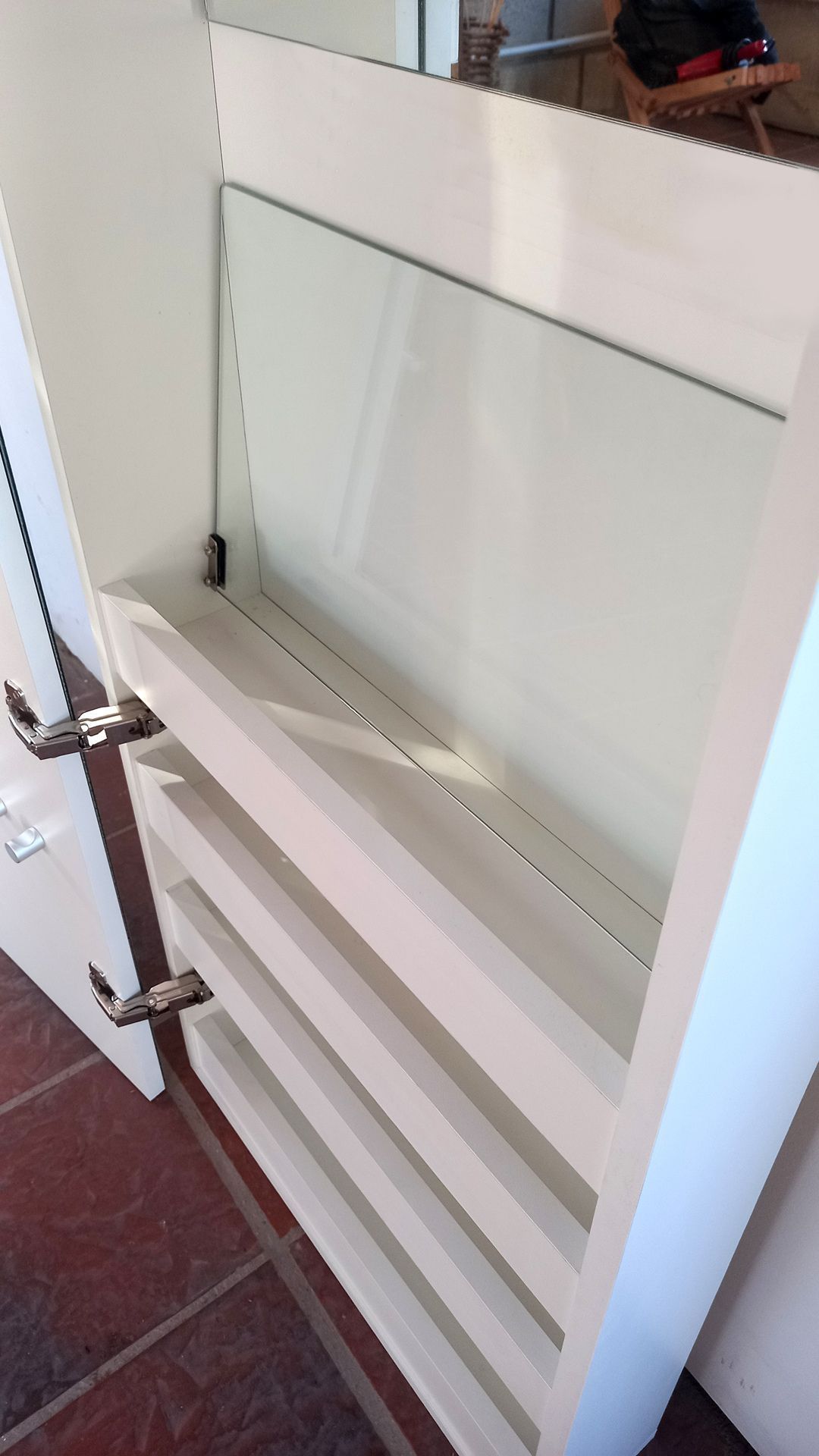 Primer plano de una bisagra plateada para armario montada en un panel de puerta blanco.