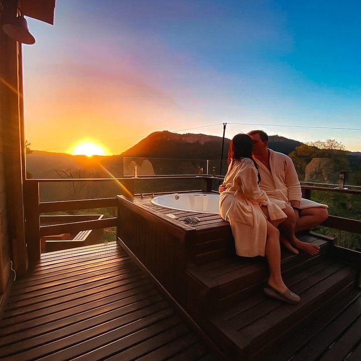 Um homem e uma mulher estão sentados em um deck próximo a uma jacuzzi ao pôr do sol.