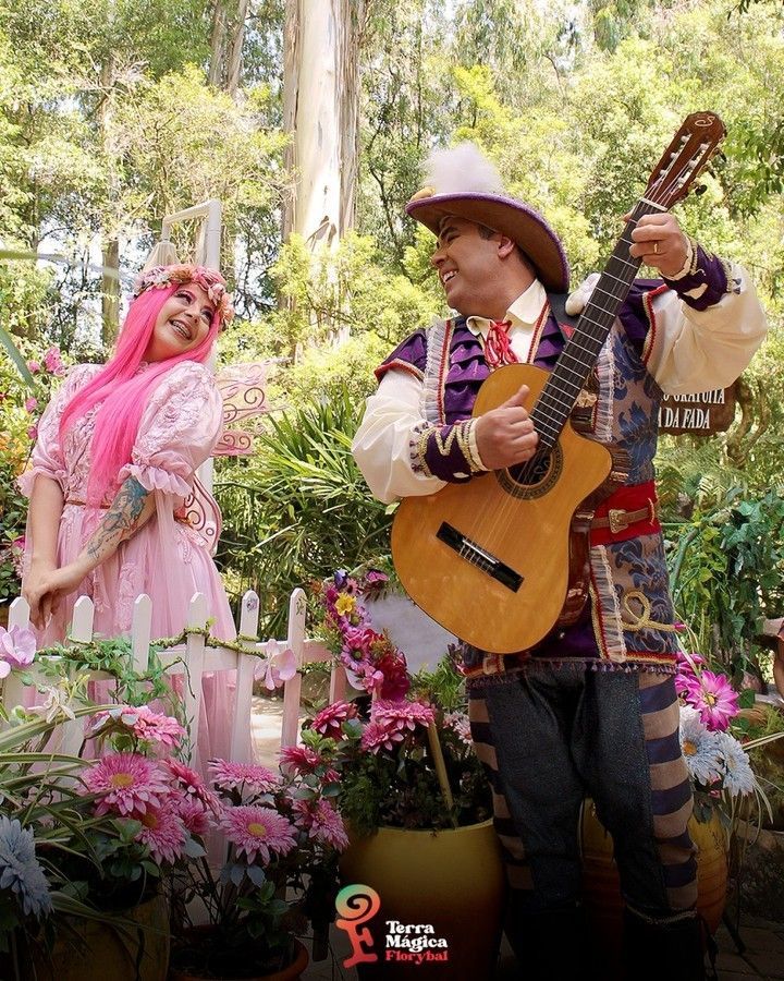 Um homem está tocando violão ao lado de uma mulher de vestido rosa.