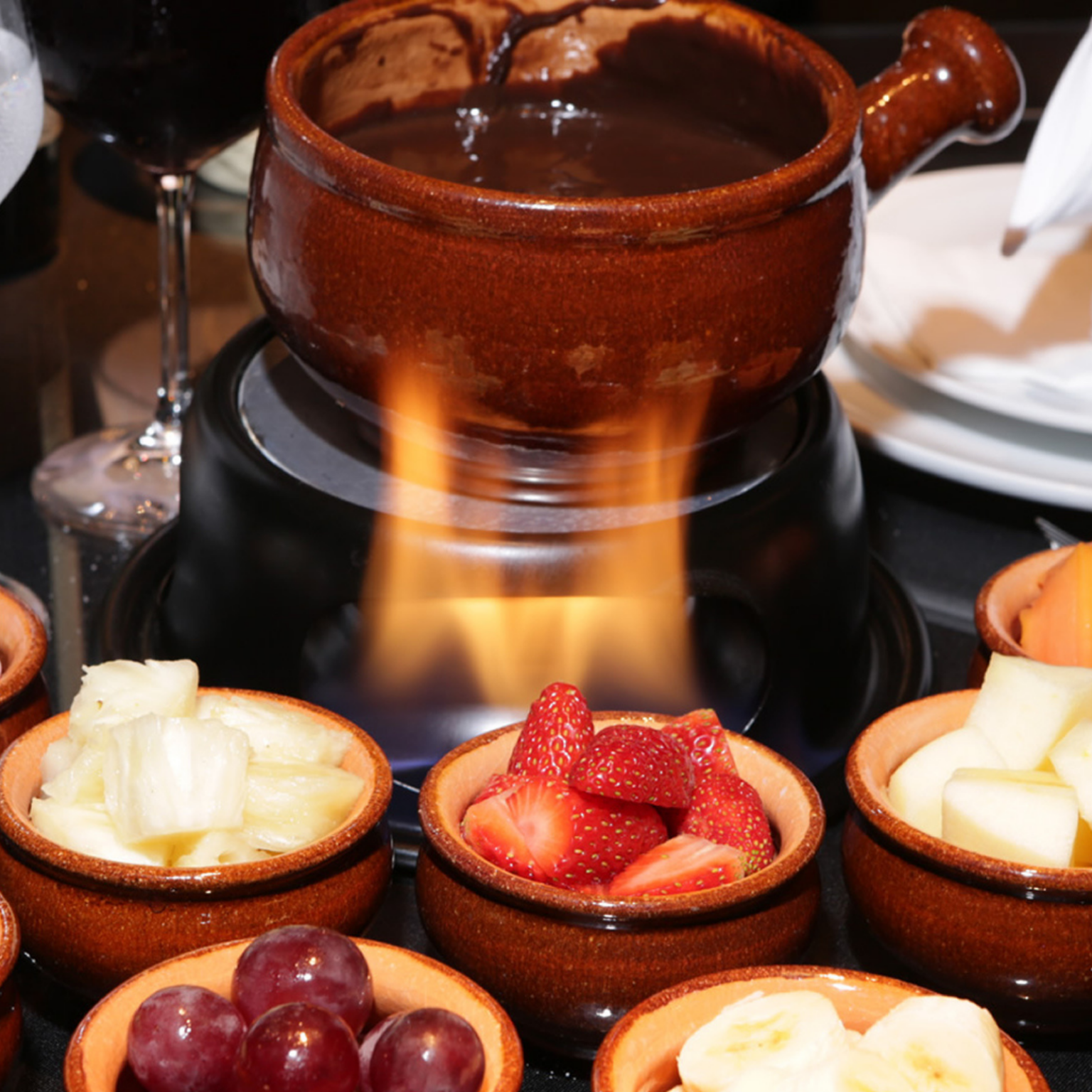 Um pote de fondue de chocolate rodeado por tigelas de frutas