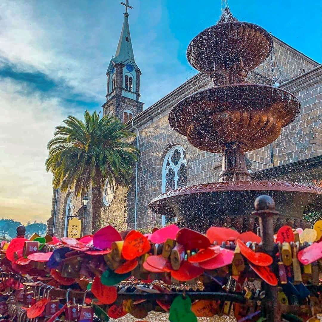 Há uma fonte em frente a uma igreja com uma torre do relógio ao fundo.