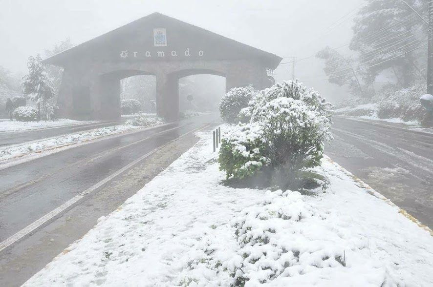 Uma estrada nevada com um prédio ao fundo e árvores cobertas de neve.