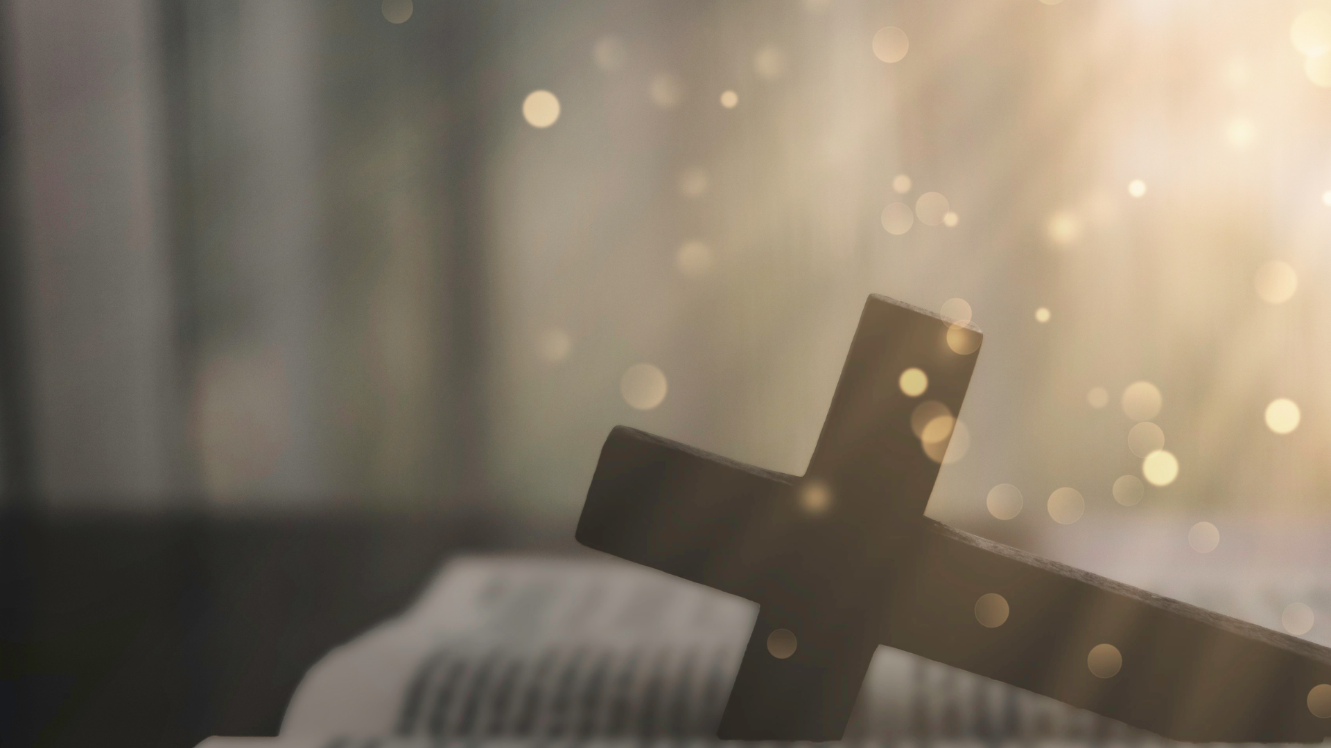 Wooden cross resting on an open book, with soft light and bokeh in the background.