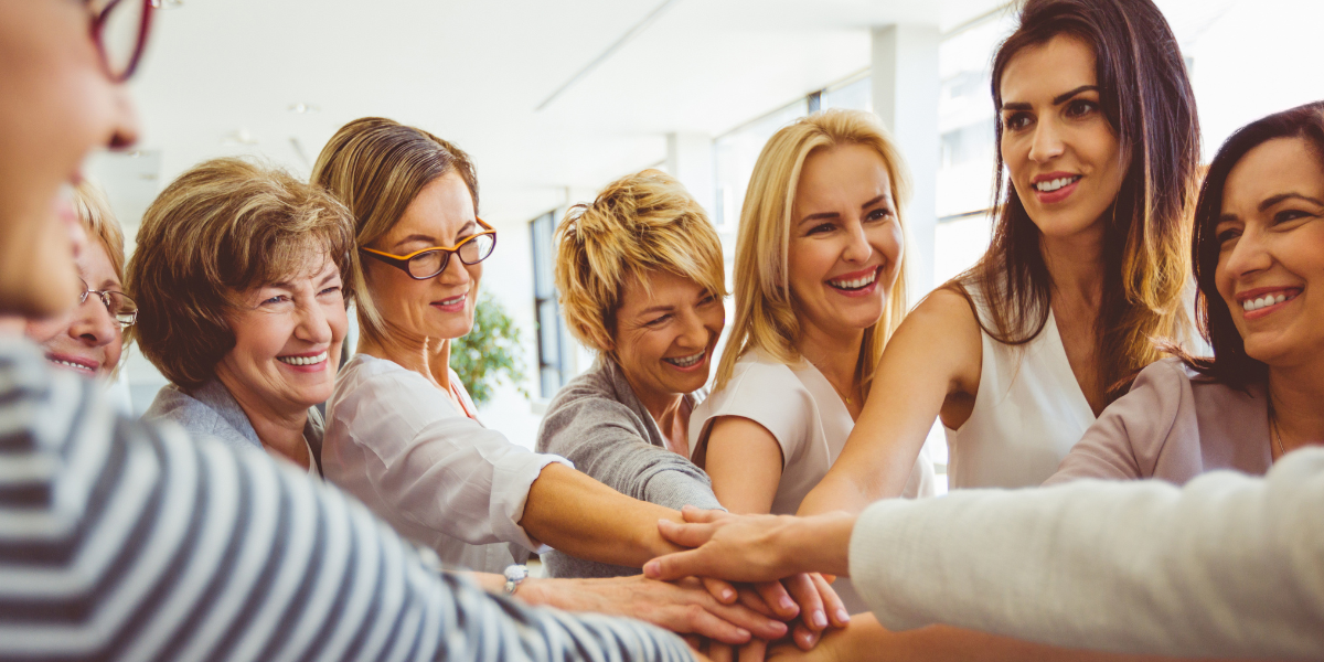 A group of women with hands stacked in unity, smiling.
