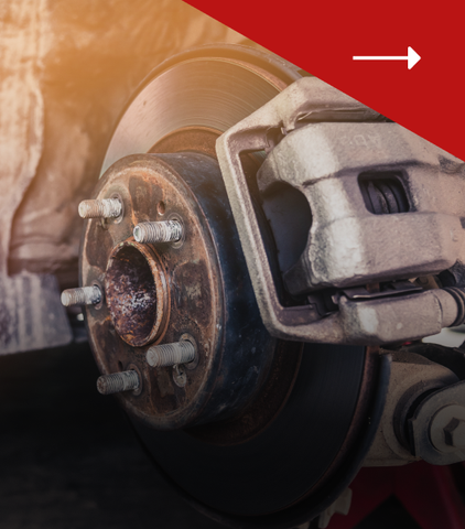 A close-up of a car's disc brake system with a brake caliper mounted over a circular rotor and wheel hub with studs.