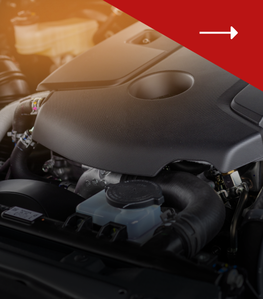 A close-up view of a car engine compartment with a black engine cover and a translucent fluid reservoir.