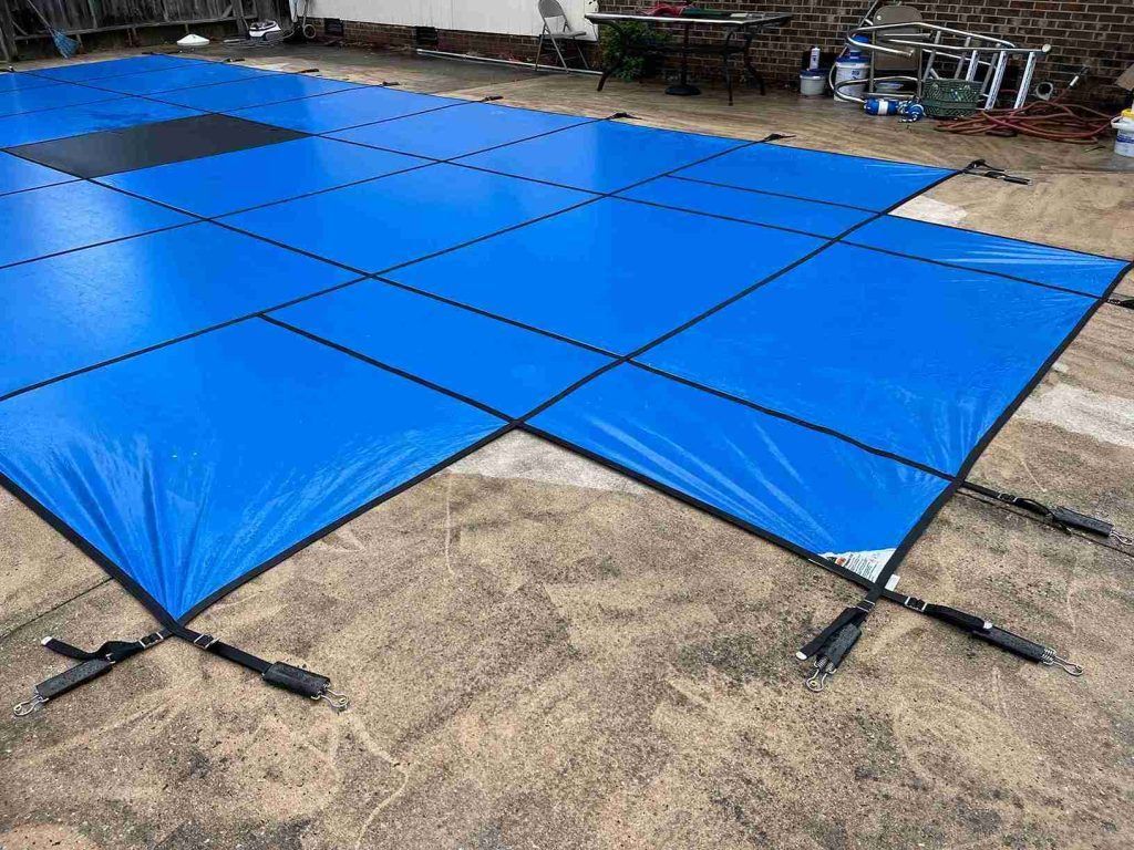 A blue swimming pool cover is sitting on top of a dirt ground.