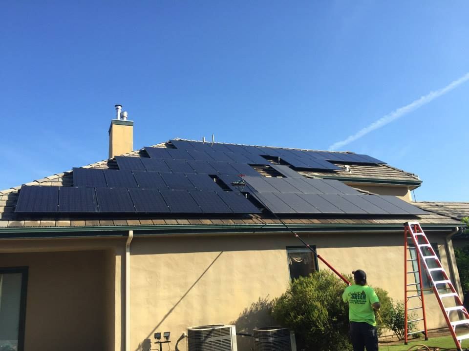 A man is standing on a ladder in front of a house with solar panels on the roof.
