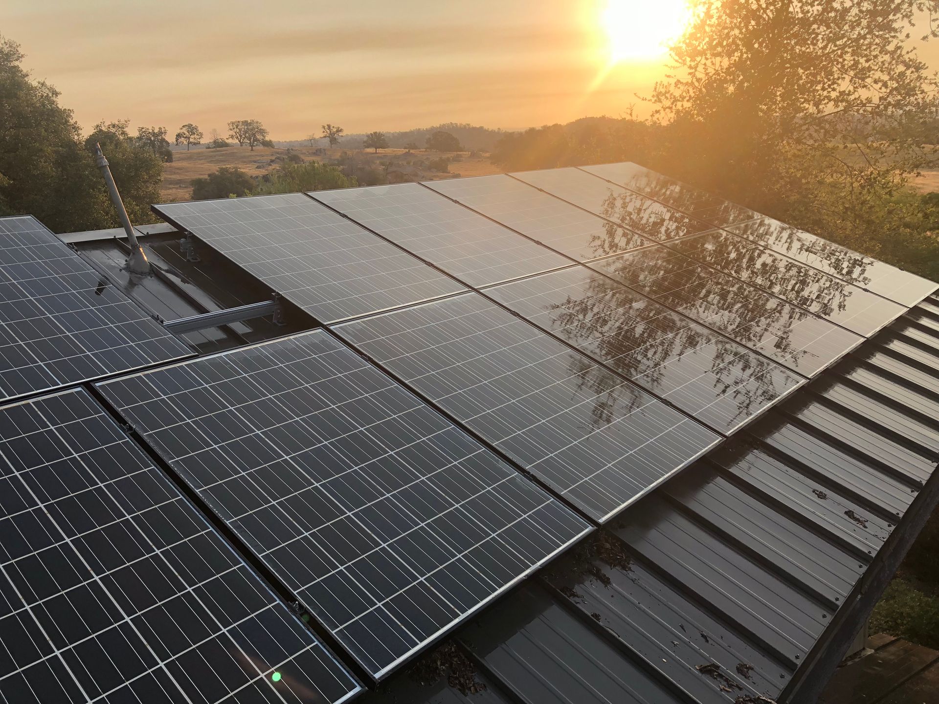The sun is setting behind the solar panels on the roof