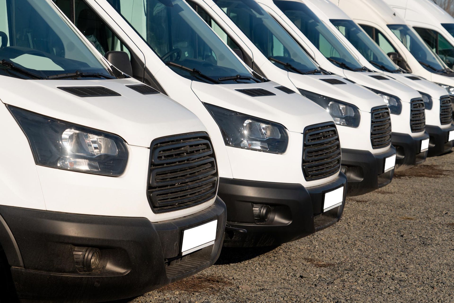 A row of white vans are parked in a parking lot.