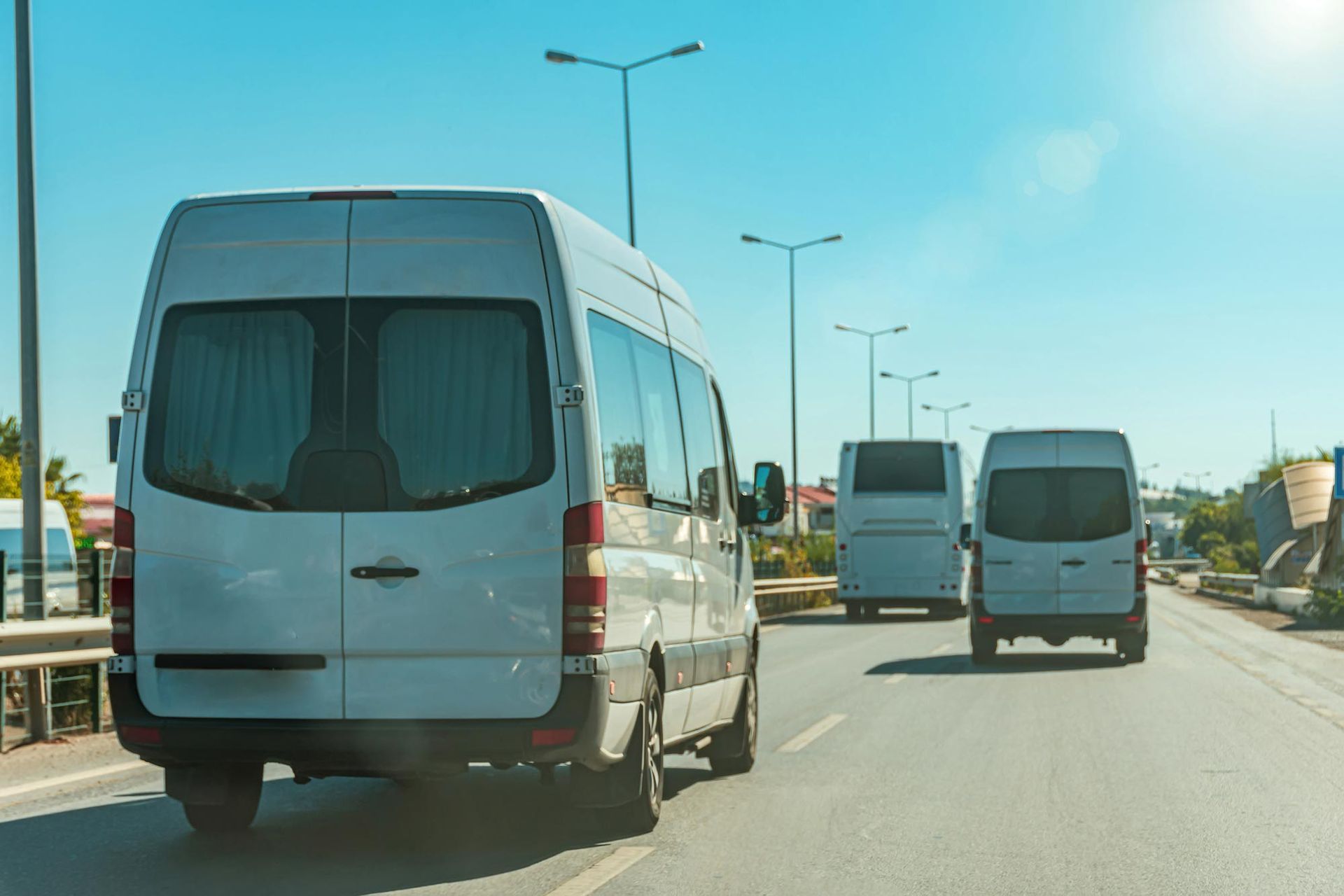 A row of white vans are driving down a highway.