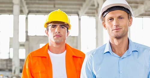 Two construction workers wearing hard hats are standing next to each other in a building.