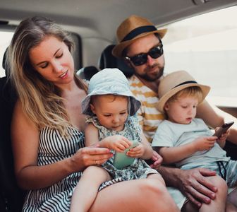 A family is sitting in the back seat of a car looking at their phones.