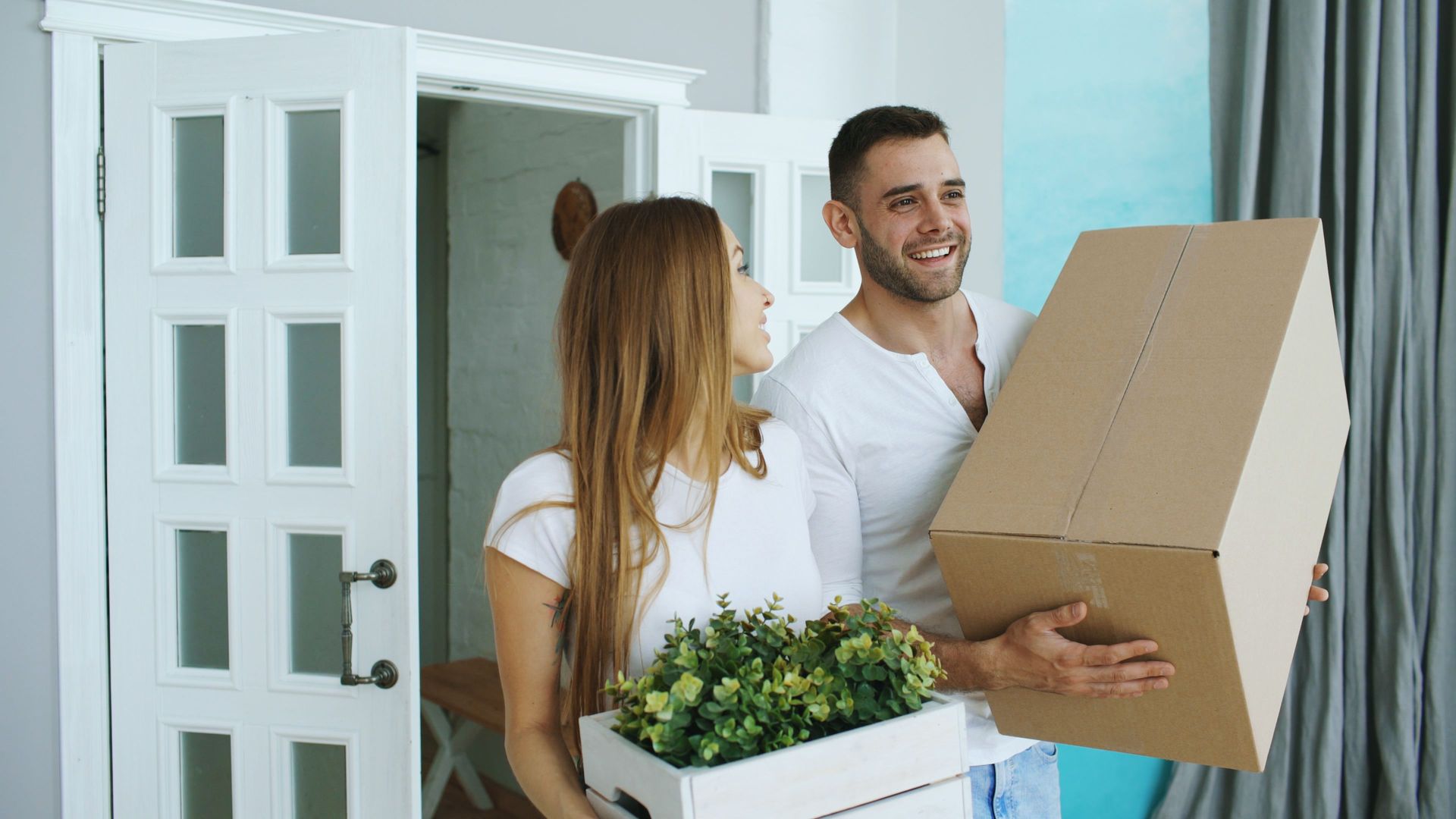 Happy newlywed couple carrying a box into their first North Texas home after combining their insuran
