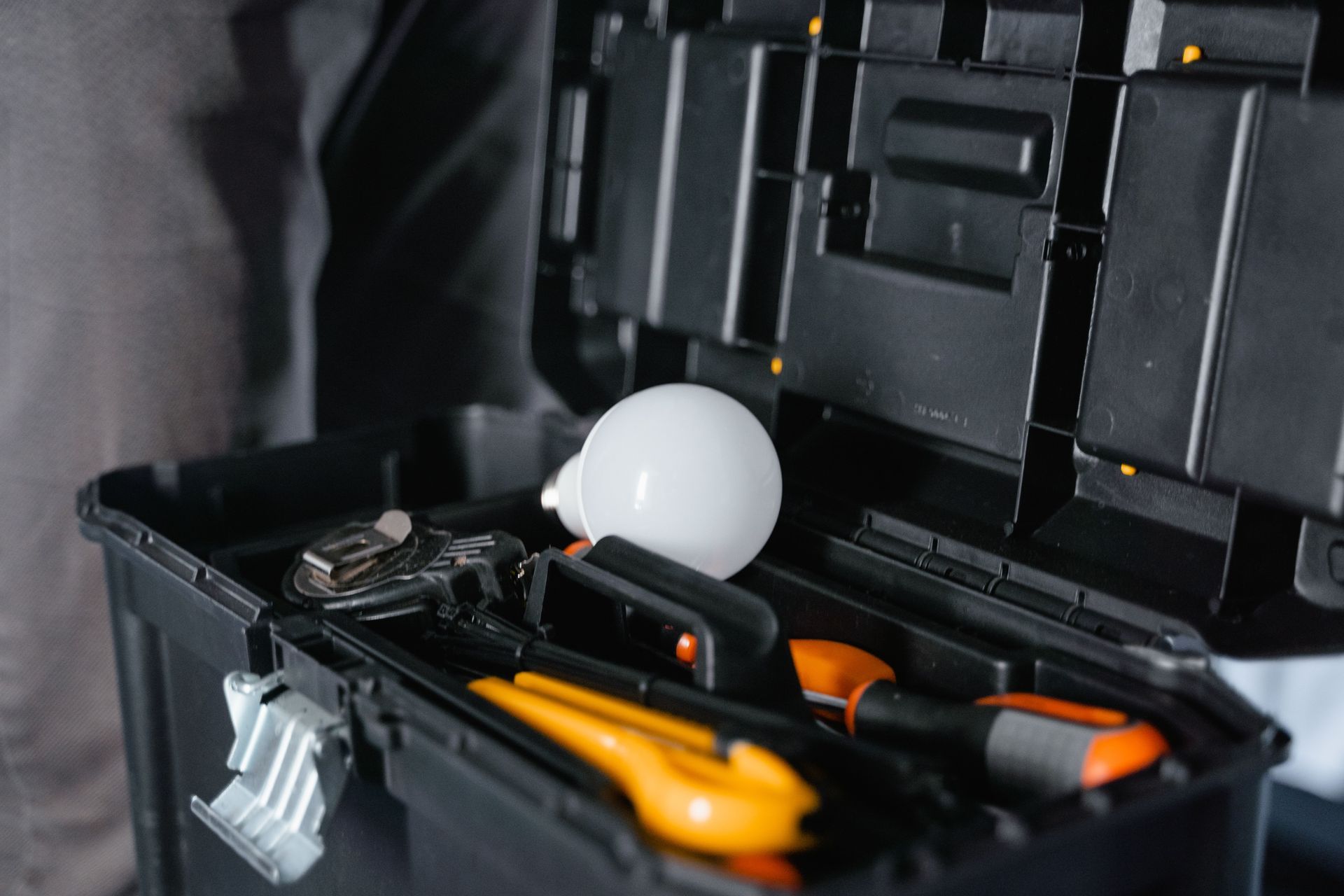 Open tool box with assorted hand tools and a white light bulb inside
