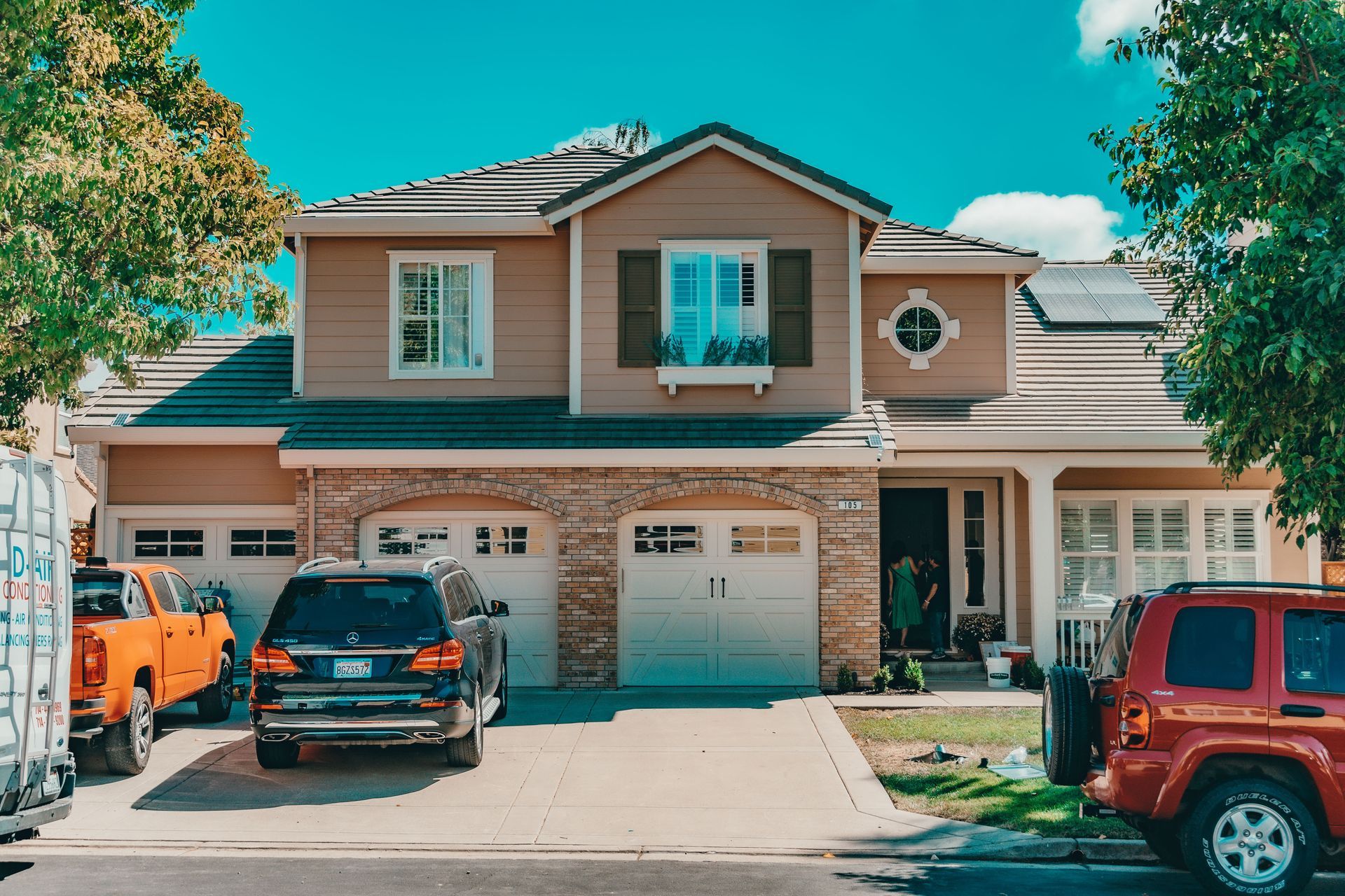 A suburban North Texas home with a tile roof and cars in the driveway under a bright, hot summer sky