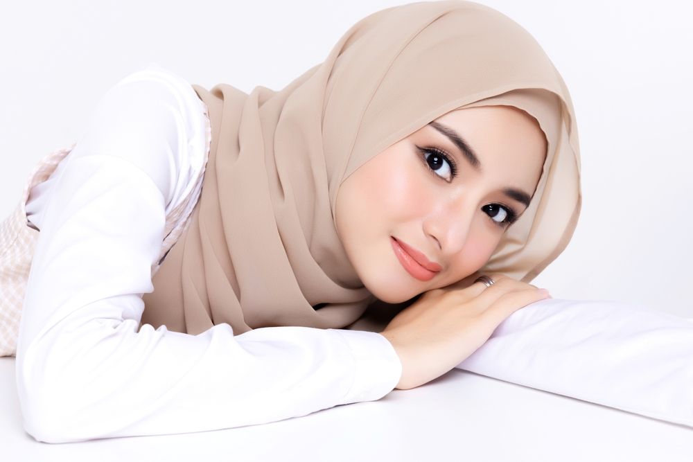 A woman wearing a hijab is laying on a bed