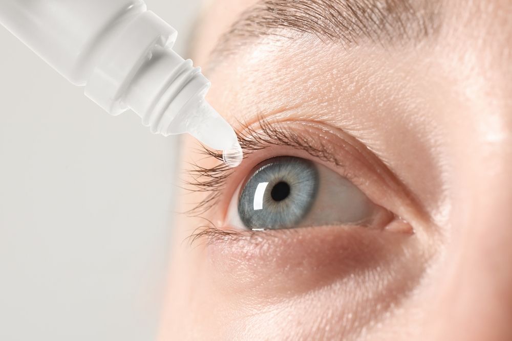 A woman is applying eye drops to her eye.