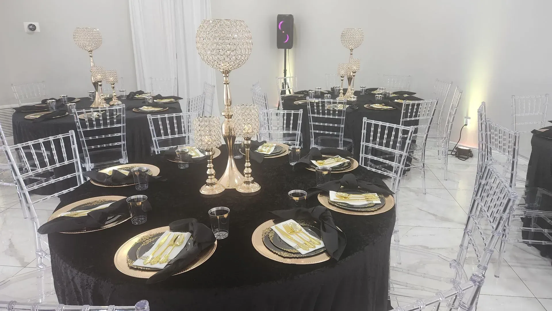 Elegant event tables set with black tablecloths, gold accents, and clear chairs.