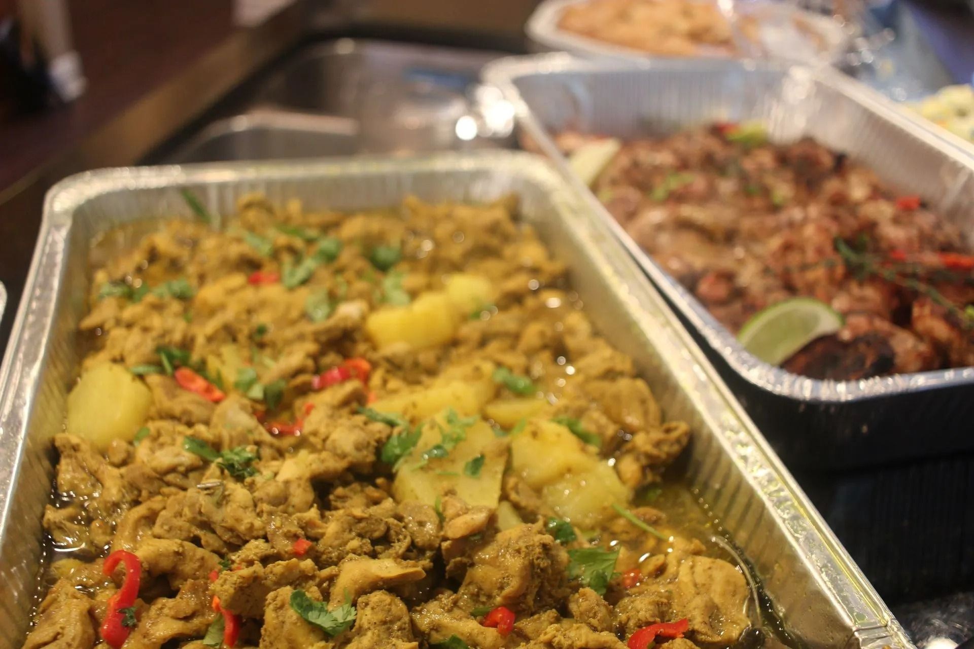 Trays of Caribbean food: curried chicken and potatoes, shrimp, and other dishes.