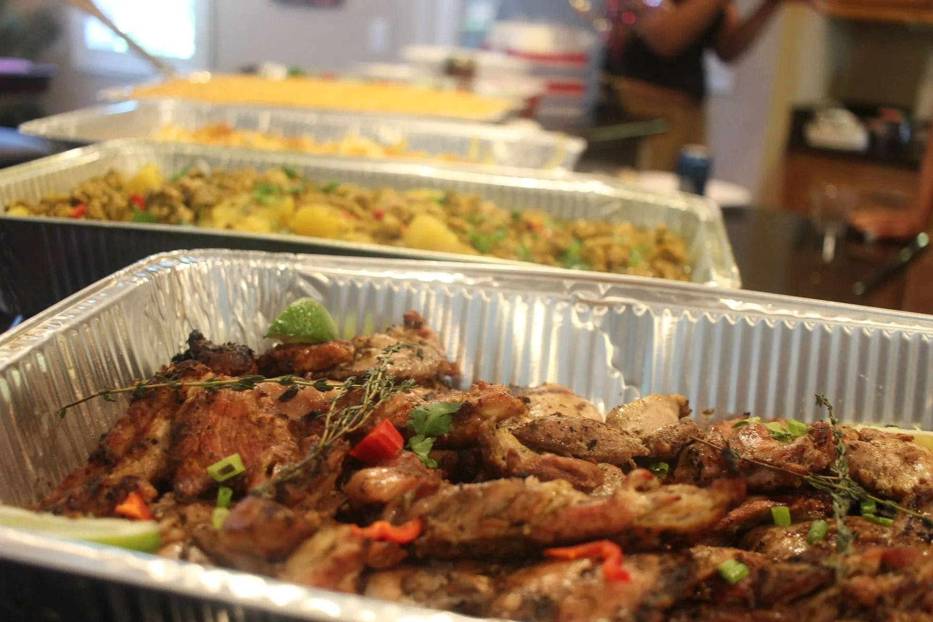 Buffet of several dishes in foil trays, including meat, rice, and vegetables.