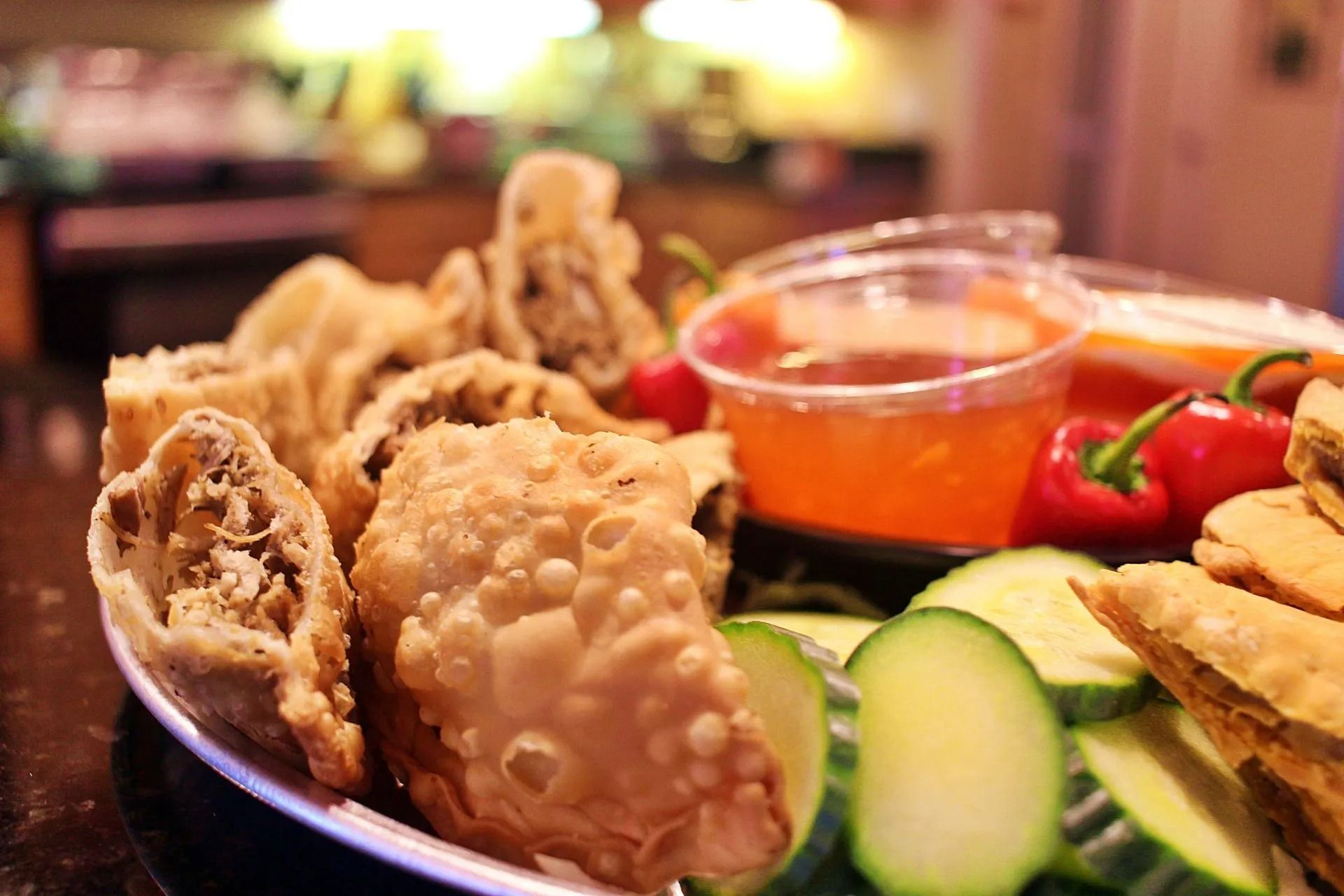 Plate of fried dumplings with dipping sauce and cucumber slices.