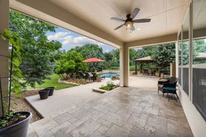 A large patio with a ceiling fan and a pool in the background.