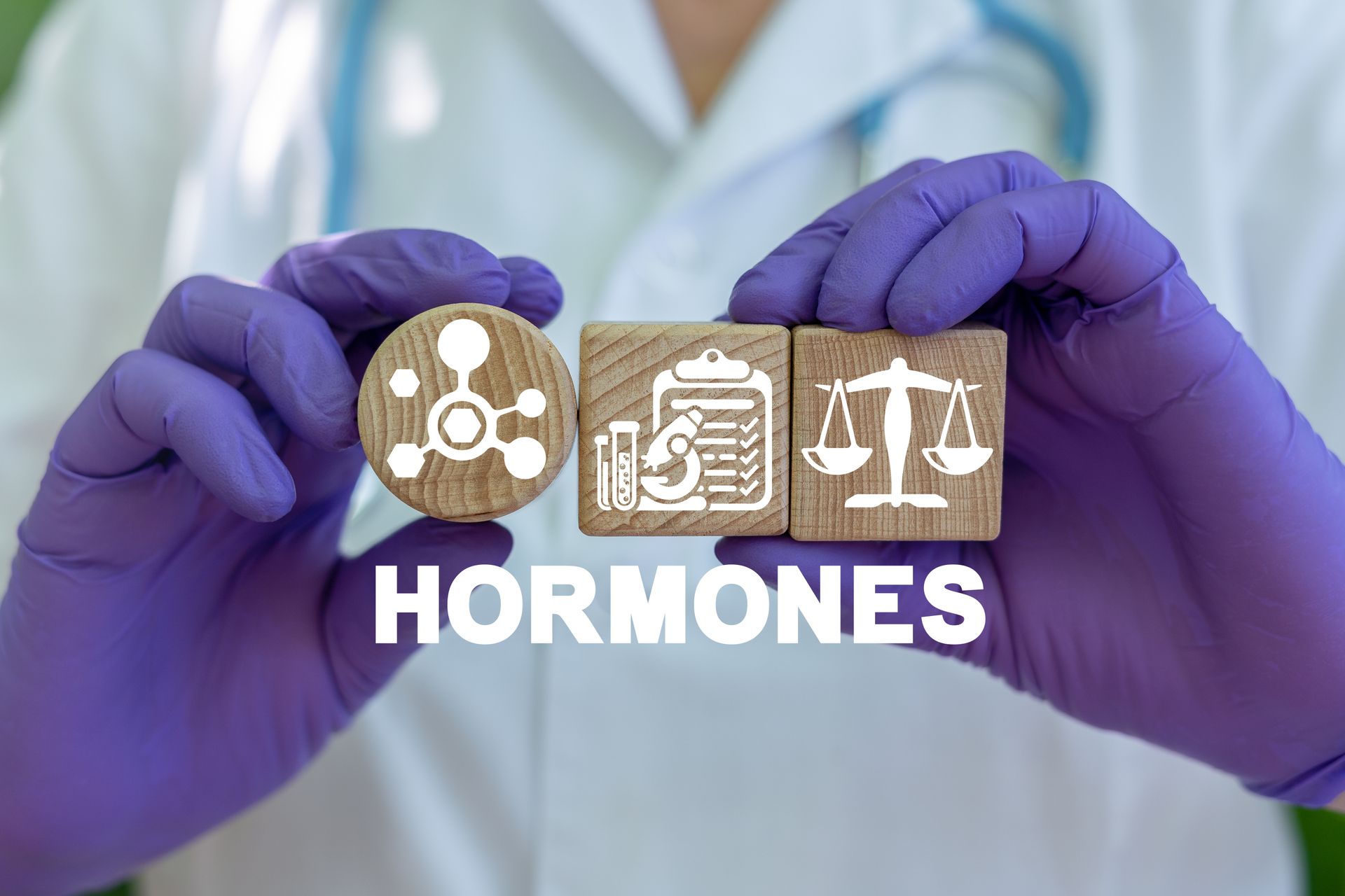 Gloved hands holding “HORMONES” text with medical icons in a clinical setting