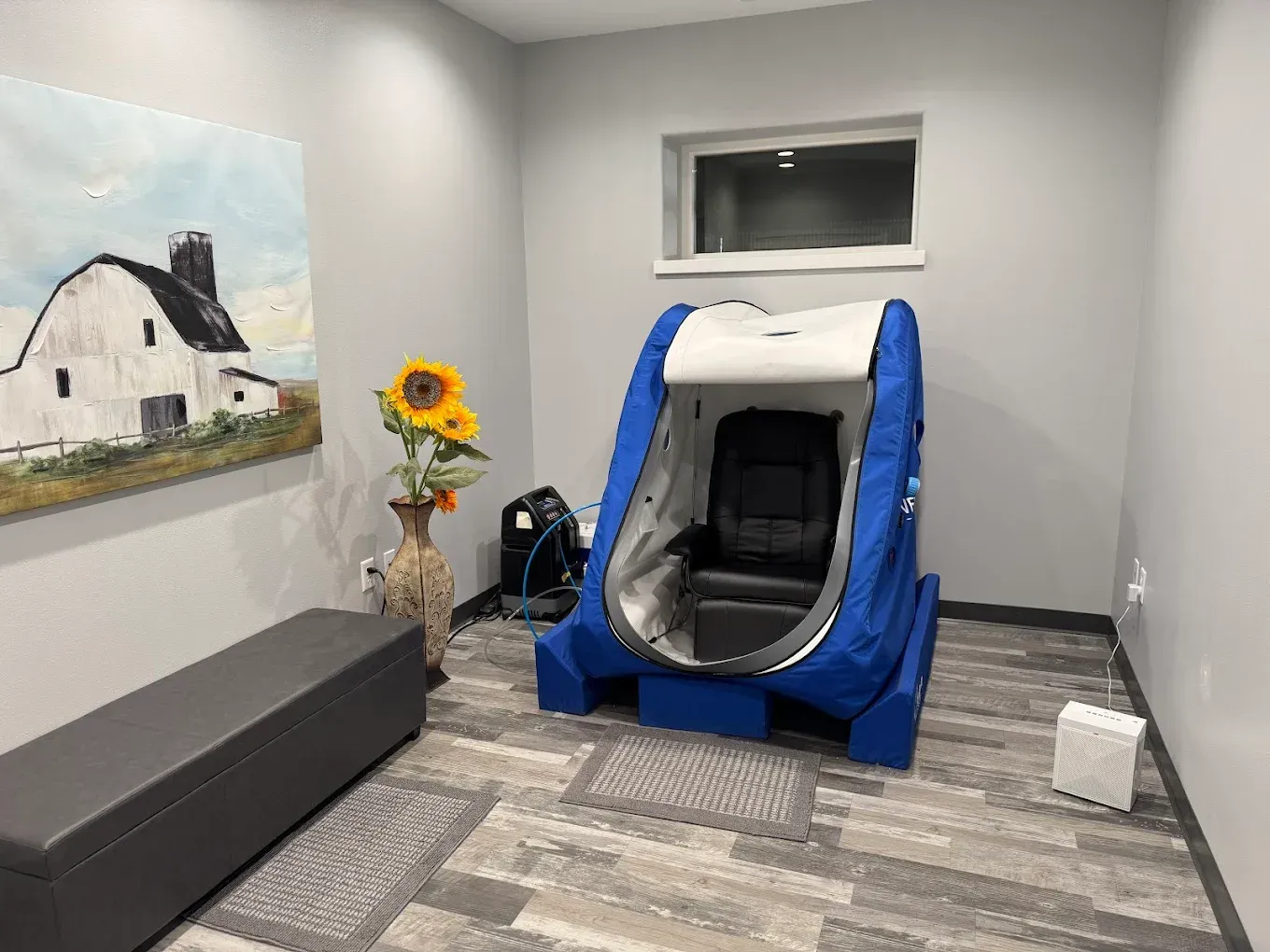 Small room with a blue-and-white massage chair, bench, sunflower vase, and wall art.