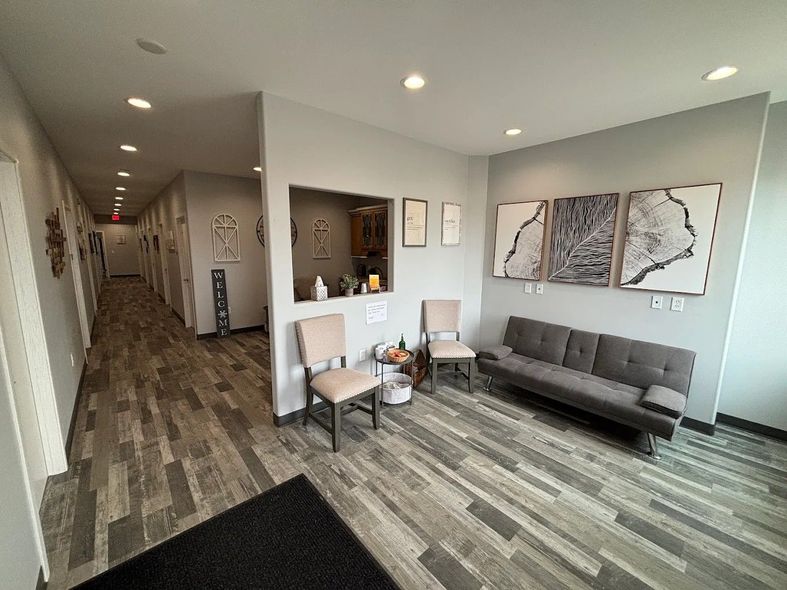 Modern office lobby with gray sofa, chairs, wall art, and long hallway with wood-look flooring